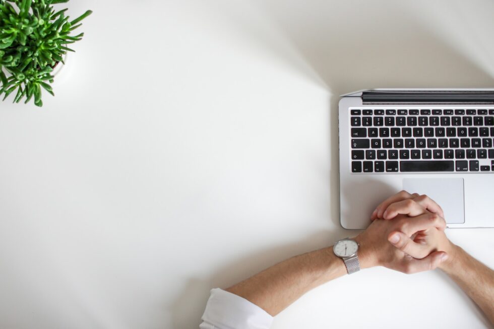 someone waiting with their hands together next to a laptop because of slow website speed and a plant